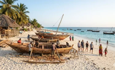 A dynamic horizontal documentary photograph capturing the unique energetic atmosphere of Nungwi beach, Northern tip of Zanzibar, during the breezy late afternoon golden hour. It features multiple local Swahili craftsmen building traditional large wooden dhow boats on the sand with hand tools, surrounding by construction materials and raw wood hulls. A lively social beach scene with local women in 'kangas', children playing, and international tourists observing unfolds nearby. Anchored weathered dhow boats are silhouetted against the rising sun out on the deep turquoise Indian Ocean. A rustic beach bar and palm-thatch structures are under mature coconut trees. Natural golden daylight illuminates the entire scene.