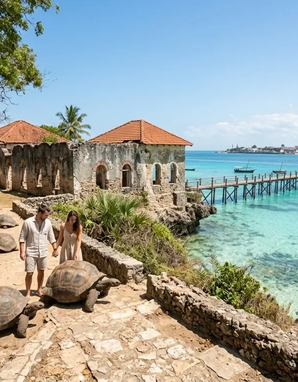 A dynamic horizontal documentary photograph capturing the unique historical and natural environment of Prison Island (Changuu), off the coast of Stone Town, Zanzibar, during a bright afternoon. It features massive Aldabra Giant Tortoises, weathered coral-rag limestone ruins with arched windows and tile roofs, a long wooden pier over shallow crystal-clear turquoise water, anchored traditional dhow boats, dense coastal vegetation, and the distant Stone Town skyline. Natural daylight filters through trees.